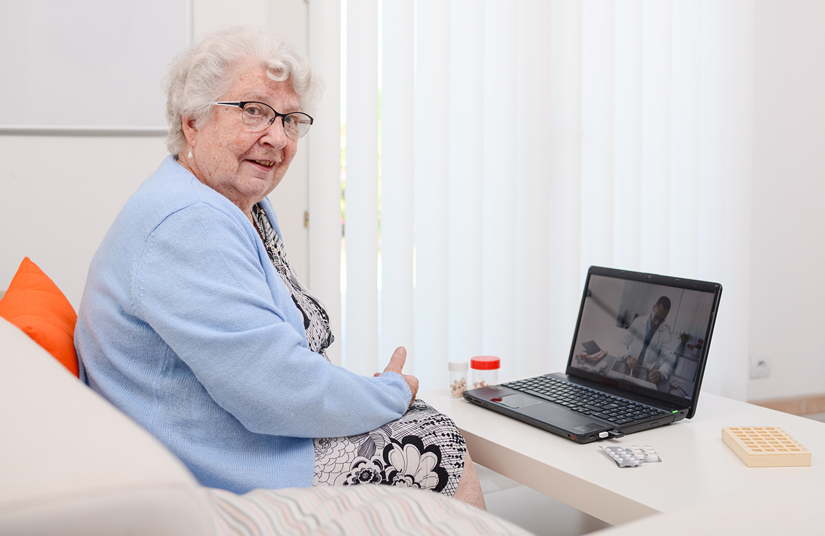 An elderly lady with glasses using her computer to access telemedicine.
